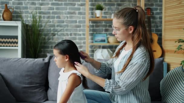 Cuidar a la madre es cepillar el pelo de las hijas cuidando a un niño hermoso en casa — Vídeos de Stock