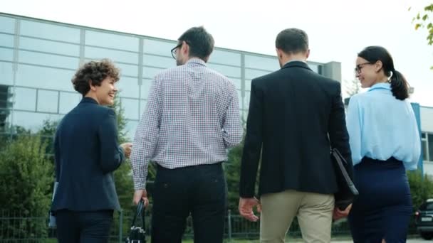 Back view of group of young businesspeople walking to office center talking — Stock Video