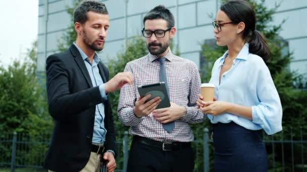 Slow motion of male and female colleagues talking and using tablet outside in city — ストック動画