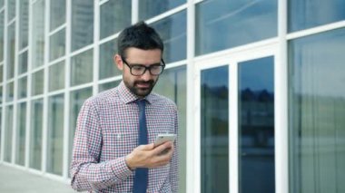 Neşeli ofis çalışanı akıllı telefon kullanarak mesaj atıyor. Sokakta gülüyor.