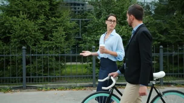 Happy girl and guy colleagues talking walking along city street, man pushing bicycle — ストック動画