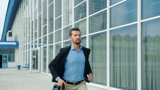 Mouvement lent de beau jeune homme courant avec mallette le long de l'immeuble de bureaux — Video