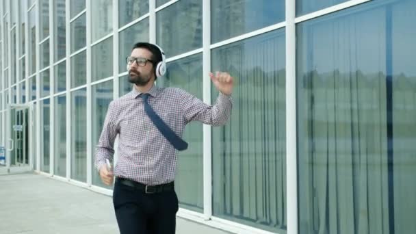 Movimiento lento de emprendedor alegre bailando al aire libre usando auriculares — Vídeo de stock