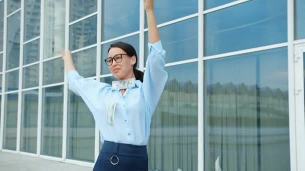 Беззаботная деловая женщина танцует за пределами офисного здания, бросая деньги веселясь — стоковое видео