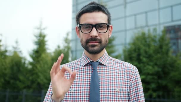 Впевнений підприємець, що показує жест гарячої руки, посміхаючись на відкритому повітрі біля офісного центру — стокове відео