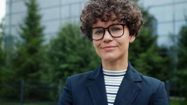 Chica ambiciosa sonriente en traje y gafas de pie en la ciudad cerca del edificio de oficinas — Vídeos de Stock