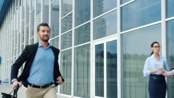 Empresario sonriente corriendo en la calle de la ciudad al edificio de oficinas sosteniendo maletín — Vídeos de Stock