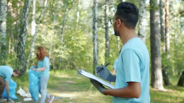 Retrato de homem árabe voluntário fazendo papelada durante a limpeza do parque no verão — Vídeo de Stock