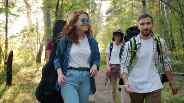 Dolly colpo di turisti ragazze e ragazzi che camminano nella foresta portando zaini parlando — Video Stock