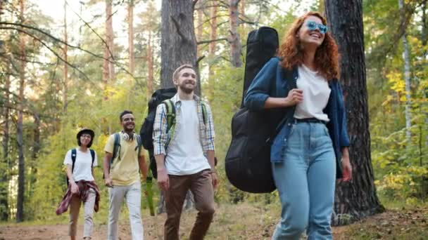 Vidám ifjúsági túrázók hátizsákkal, akik az erdőben sétálnak mosolyogva, nyáron utaznak — Stock videók
