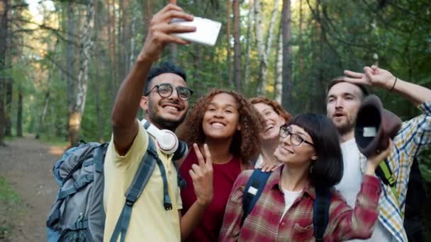 Ormanda el hareketleriyle poz vererek selfie çeken neşeli gençlerin yavaş hareketi. — Stok video
