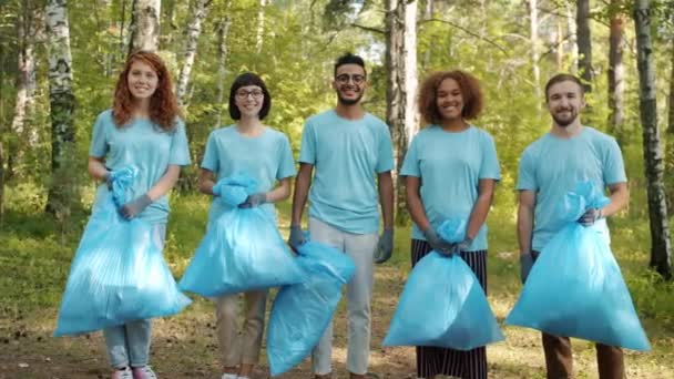 Portret van jonge vrijwilligers in het bos met vuilniszakken die buiten glimlachen — Stockvideo