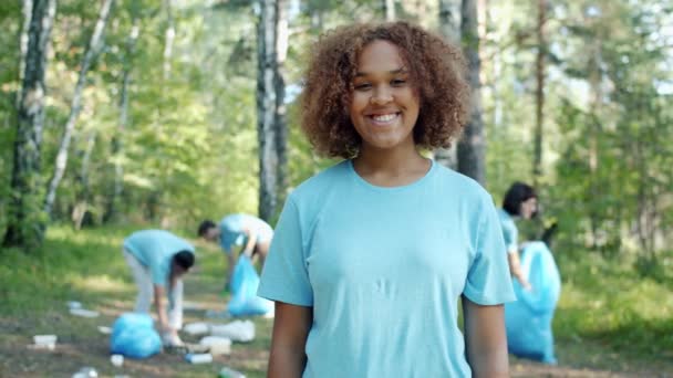Porträtt av glad afro-amerikansk flicka i frivillig uniform i förorenad skog — Stockvideo