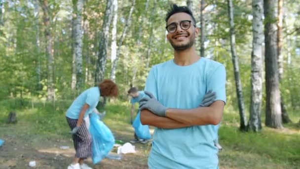 Retrato del alegre hombre árabe voluntario en uniforme sonriendo en un bosque contaminado — Vídeo de stock
