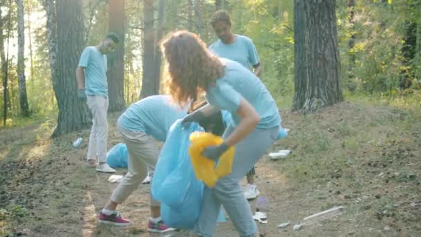 Jóvenes voluntarios recogiendo botellas de basura y plástico del suelo en bosques contaminados — Vídeos de Stock