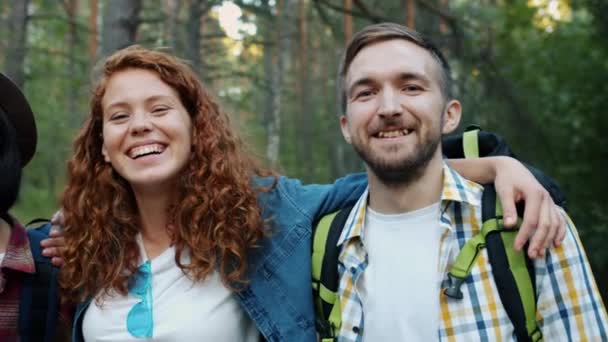 Портрет смеющихся девушек и парней в лесу, которые весело обнимаются, смотря в камеру — стоковое видео