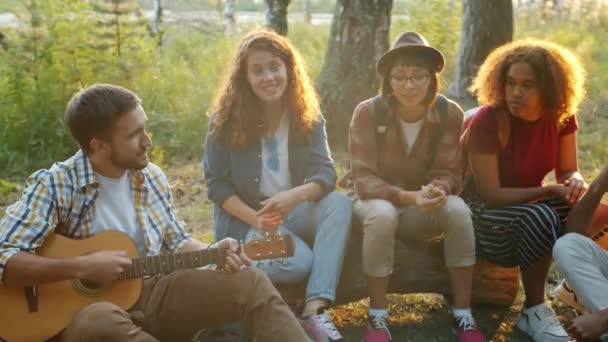 Multiethnische Gruppe von befreundeten Touristen, die im Wald Gitarre spielen und Lieder singen — Stockvideo