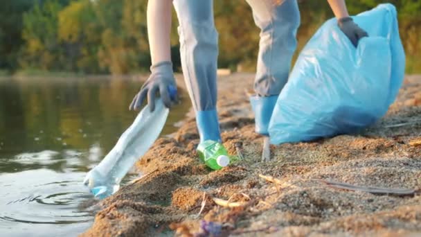 Primer plano de piernas y manos femeninas recogiendo basura en la orilla del lago en verano — Vídeo de stock