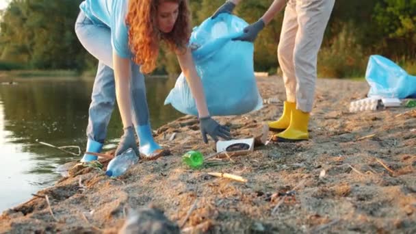 Tilt-up of two female eco activists picking trash on the beach working together — 图库视频影像