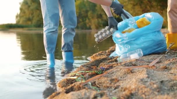 Tiro bajo de mujeres voluntarias limpiando la orilla del río de basura usando bolsa de basura — Vídeos de Stock