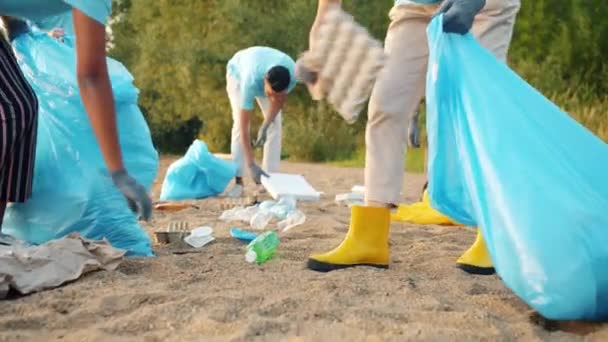 Laag schot van de jeugd vrijwilligers verzamelen afval op de oever van het meer het oprapen van afval — Stockvideo