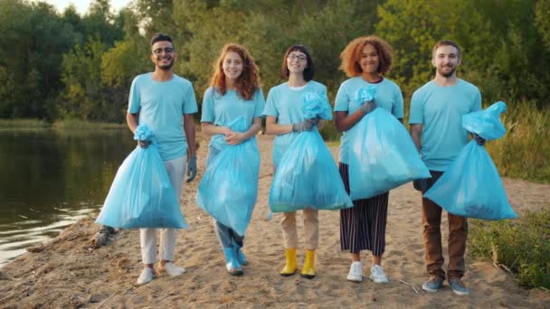 清澈湖岸背垃圾袋的多民族志愿者的画像 — 图库视频影像