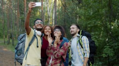 Kızlar ve erkekler ormanda selfie çekiyorlar yaz günü sırt çantalarını tutarak eğleniyorlar.