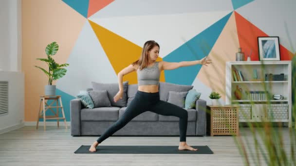 Good-looking young woman practicing yoga in apartment stretching body and arms — ストック動画