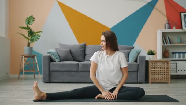 迷人的女孩在瑜伽垫上做伸展运动，在家里的地板上放松 — 图库视频影像