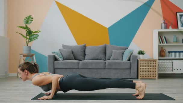 Atlética dama ejercitando en casa en posición tablón luego haciendo yoga hacia abajo perro asana — Vídeos de Stock
