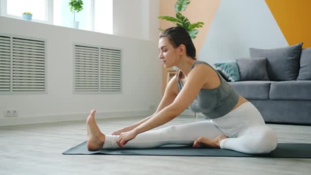 Carefree girl bending to one leg developing flexibility doing yoga alone at home — ストック動画