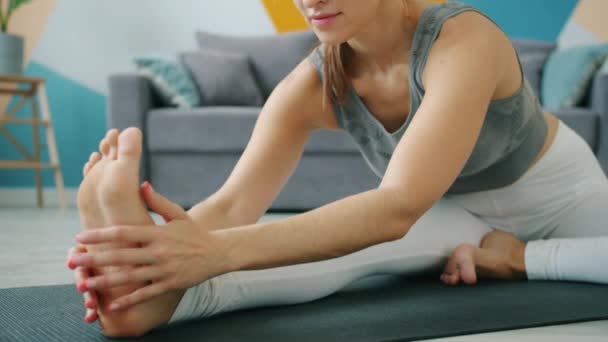 Låg bild av flexibel ung kvinna som gör yoga hemma böja till foten på mattan — Stockvideo