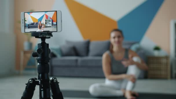 Женщина блоггер запись видео со смартфона делает йогу дома, сосредоточиться на экране — стоковое видео