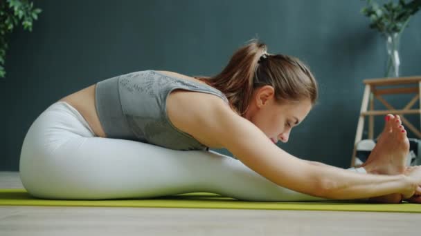 Niski strzał ładnej dziewczyny ćwiczącej do przodu zginać siedzi na macie do jogi w nowoczesnym studio — Wideo stockowe