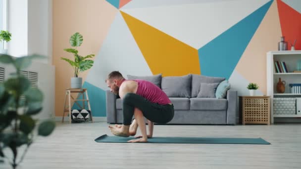 Male yoga student exercising at home doing arms balancing asana on rubber mat — ストック動画