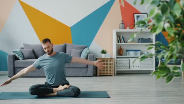 Joven serio haciendo yoga en casa estirando cuerpo en posición de loto sobre estera — Vídeos de Stock