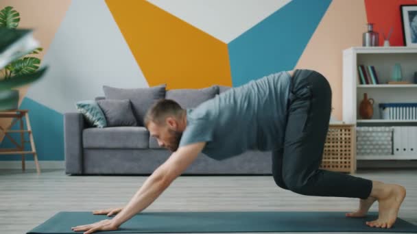 Медленное движение бородатый человек делает балансировки йоги упражнения, работающие в доме — стоковое видео