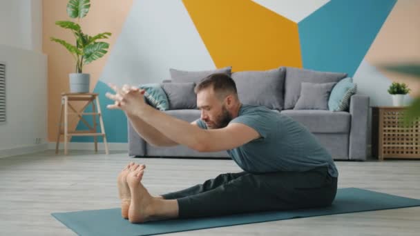 Flexibele man stretching lichaam in zittende positie doen naar voren buigen naar de benen — Stockvideo