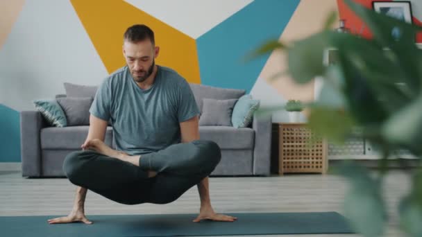 Bărbat cu barbă ridicând corpul cu brațele în poziția de lotus făcând yoga acasă — Videoclip de stoc