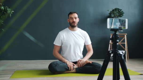 Fešák muž vlogger nahrávání video tutorial v jóga studio dělá asanas — Stock video