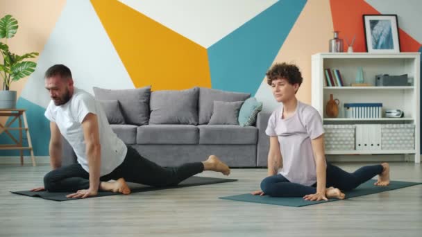 Unga par man och kvinna som tränar yoga hemma tillsammans på mattor — Stockvideo