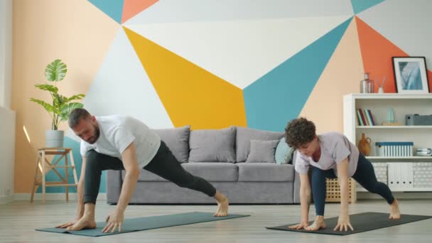 Woman and man working out at home doing yoga together synchronously on mats — ストック動画