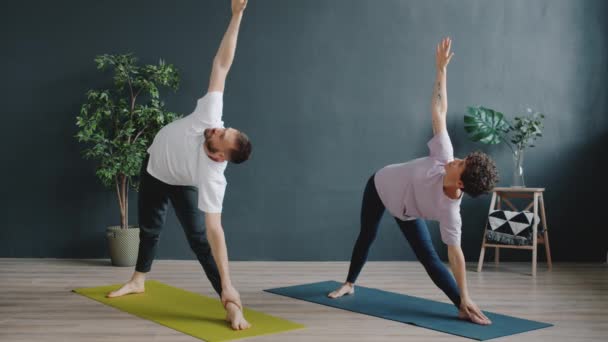 Man instructeur onderwijs vrouwelijke yoga student in gezellige studio, mensen doen asanas — Stockvideo