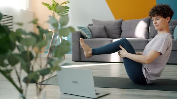 Гнучка дівчина вчить йогу онлайн за допомогою ноутбука дивитися підручник в Інтернеті — стокове відео