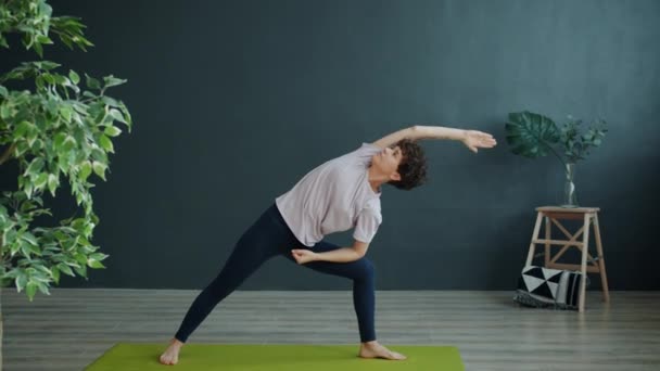 Active young woman doing yoga in studio exercising alone indoors in cozy room — ストック動画