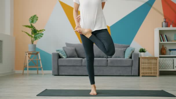 Snella giovane donna in equilibrio su un piede durante la pratica individuale di yoga a casa — Video Stock