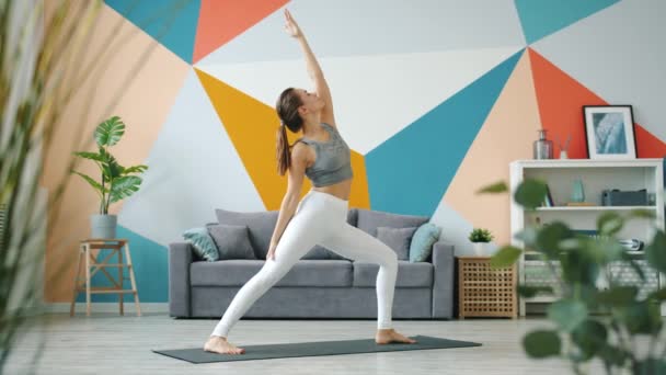 Ehrfürchtige junge Frau beim Balancieren und Dehnen von Yoga-Asanas auf dem Boden zu Hause — Stockvideo