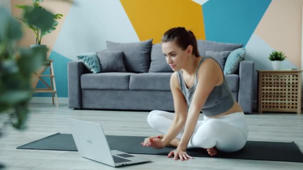 Jovem mulher fazendo ioga assistindo tutorial usando laptop no apartamento no tapete — Vídeo de Stock