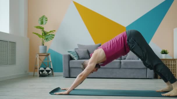 Knappe jongeman doet yoga thuis gericht op de praktijk in appartement — Stockvideo