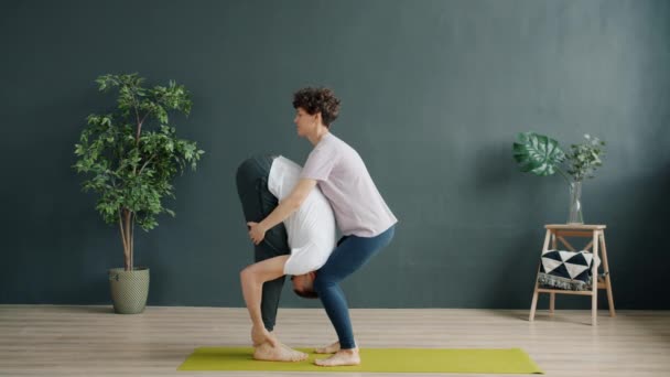 Profesora de yoga y alumna haciendo yoga en pareja en el gimnasio, chica levantando chico hablando — Vídeo de stock